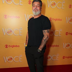 Maurício Mattar adota a estética all black em uma combinação minimalista de camiseta básica preta com calça reta de mesmo tom. O visual ganha presença com as tatuagens nos braços à mostra, barba grisalha alinhada e tênis escuros de solado claro