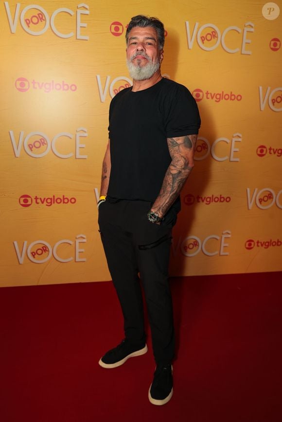 Maurício Mattar adota a estética all black em uma combinação minimalista de camiseta básica preta com calça reta de mesmo tom. O visual ganha presença com as tatuagens nos braços à mostra, barba grisalha alinhada e tênis escuros de solado claro