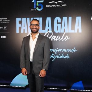 Konrad Dantas, fundador e produtor do Kondzilla, aposta em traje casual chic com costume chumbo ajustado e camisa branca social de gola aberta sem gravata. O visual moderno é arrematado por tênis casuais brancos de solado robusto e óculos de armação preta marcante