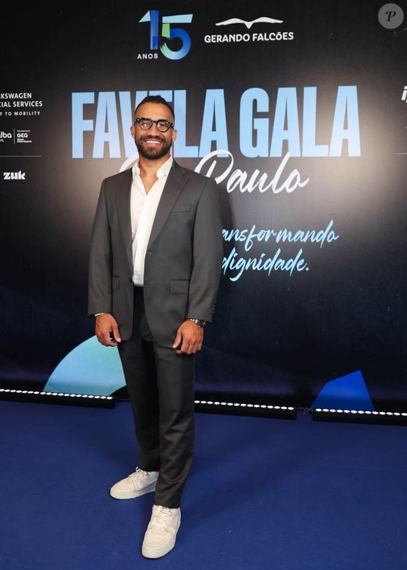 Konrad Dantas, fundador e produtor do Kondzilla, aposta em traje casual chic com costume chumbo ajustado e camisa branca social de gola aberta sem gravata. O visual moderno é arrematado por tênis casuais brancos de solado robusto e óculos de armação preta marcante