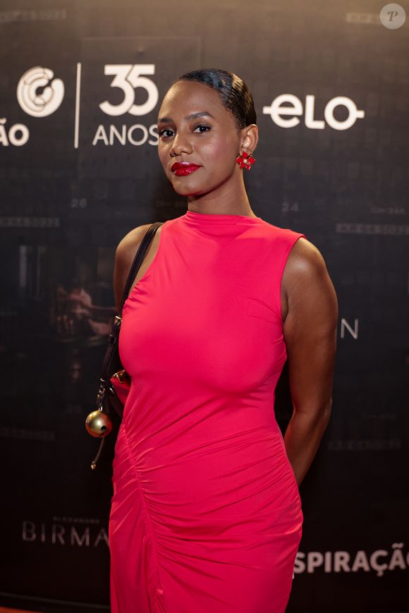 No tapete vermelho, Jéssica Ellen aposta em um visual monocromático de forte impacto, com vestido midi em tom vibrante de vermelho que valoriza a silhueta por meio de drapeados estratégicos ao longo do corpo, criando textura e movimento sutil; a peça, de gola alta e sem mangas, reforça a elegância minimalista, enquanto os acessórios seguem a mesma cartela, com sandálias de tiras finas e brilho acetinado e brincos esculturais que conversam com o look, além de uma bolsa de alça fina com detalhe metálico