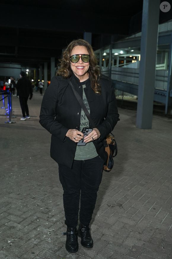 Ana Carolina: usa blazer estruturado preto sobre camiseta verde estampada, calça preta, óculos de armação grande, bolsa transversal e botas pretas com fivelas