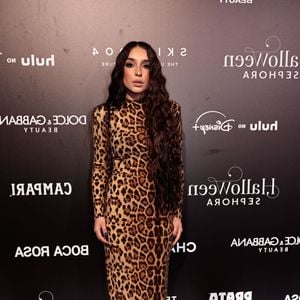 Sabrina Viana veste um vestido longo e justo ao corpo com gola alta e mangas compridas, confeccionado inteiramente em padronagem de animal print de onça clássica. O visual clean e elegante é finalizado com cabelos bem longos e ondulados soltos divididos ao meio, maquiagem suave com destaque nos olhos e unhas compridas escuras