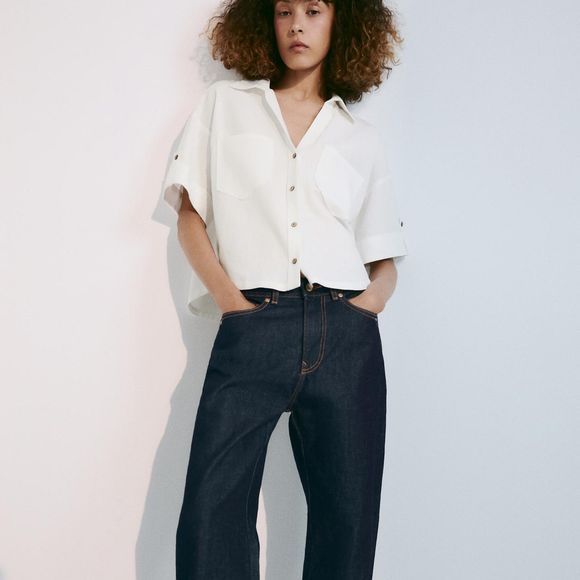 A Camisa Crop em Mistura de Linho com Botões da Zara aposta no comprimento cropped e reúne mistura de linho, decote V, mangas curtas e bolsos de patch frontais