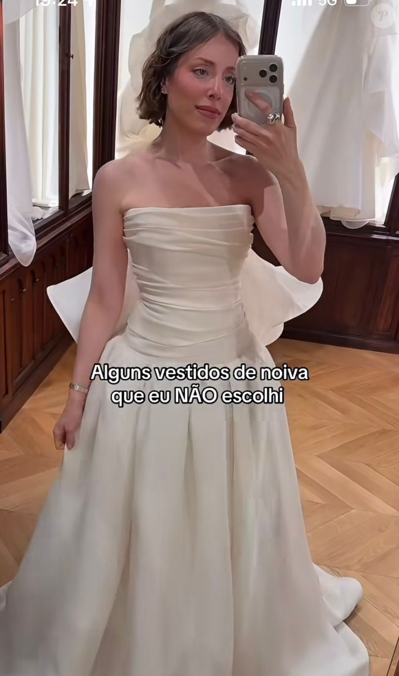 1. Tomara que caia liso com laço/volume posterior: modelo off-white de cetim/tafetá com decote tomara que caia reto, corpete com drapeado horizontal leve e cintura de corte baixo (dropped waist). A saia godê ampla possui pregas verticais marcadas, complementada por um laço ou elemento estruturado de tecido drapeado fixado na parte posterior