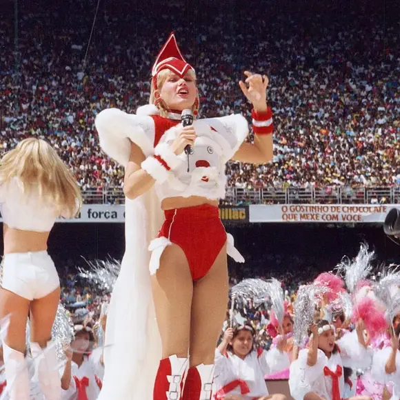 Xuxa Meneghel em mais uma produção criativa composta por capa, bota vermelha e acessório no cabelo.