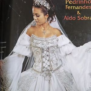 4. Vestido corset prateado

Puro drama e maximalismo! Esse vestido remete à realeza barroca, com um corpete estruturado que imita um espartilho, entrelaçado por fitas prateadas e cercado por bordados em arabescos. As mangas bufantes caídas nos ombros trazem teatralidade, enquanto a saia ampla é toda contornada por bordados rebuscados. É um vestido de presença, perfeito para a noiva que queria ser lembrada como uma verdadeira rainha.