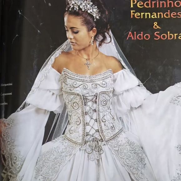 4. Vestido corset prateado

Puro drama e maximalismo! Esse vestido remete à realeza barroca, com um corpete estruturado que imita um espartilho, entrelaçado por fitas prateadas e cercado por bordados em arabescos. As mangas bufantes caídas nos ombros trazem teatralidade, enquanto a saia ampla é toda contornada por bordados rebuscados. É um vestido de presença, perfeito para a noiva que queria ser lembrada como uma verdadeira rainha.