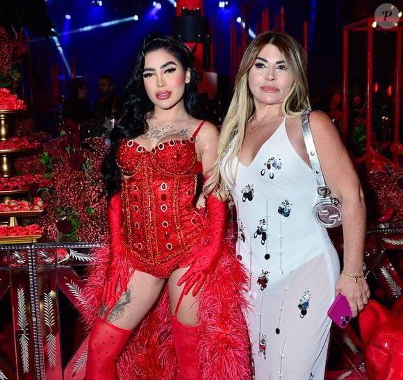 A mãe da funkeira optou por um vestido branco justo e transparente, adornado com apliques brilhantes em formato floral, complementado por uma bolsa prata da Gucci e sandália de salto. Duas gerações unidas pelo glamour na noite mais ousada do ano