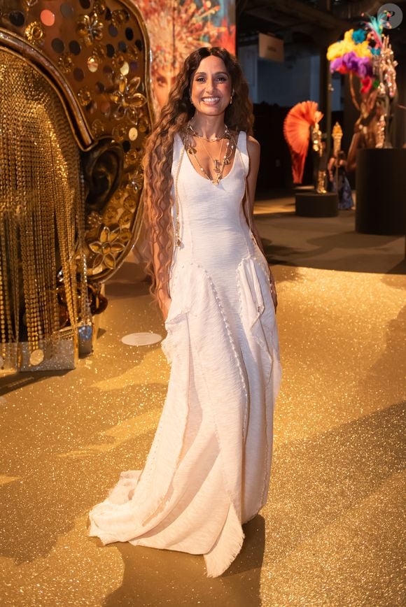 Camila Pitanga iluminou o evento com uma estética 'boho-chic' solar e sofisticada, vestindo um longo da grife Aluf em tom off-white. O vestido, confeccionado em um tecido de textura rústica que remete ao linho tramado, apresenta um decote em 'V' profundo e uma modelagem escultural com recortes verticais que terminam em barras levemente desfiadas, conferindo um ar artesanal de luxo