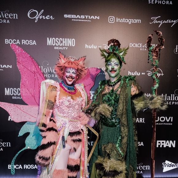 Fih e Edu, do 'Divas Depressão': o casal surge com fantasias coordenadas de inspiração na floresta e no universo felino; Fih usa um corpete rosa com brilhantes, asas de borboleta em tom rosa e turquesa, detalhes em pelagem estampada de tigre e cartola com orelhas. Edu veste uma túnica drapeada em tons de verde com texturas folhosas, perneiras felpudas de pelagem verde e preta, maquiagem felina e empunha um cajado de madeira esculpido com folhagens enroladas