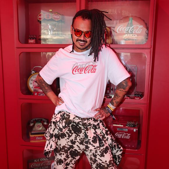 Duh Marinho traz uma proposta divertida e audaciosa de streetwear conceitual. Ele veste uma camiseta branca oversized com a estampa da marca patrocinadora combinada com macacão estampado em cow print usado com a parte superior amarrada na cintura, finalizando com óculos de lentes vermelhas e calçados em tom vibrante